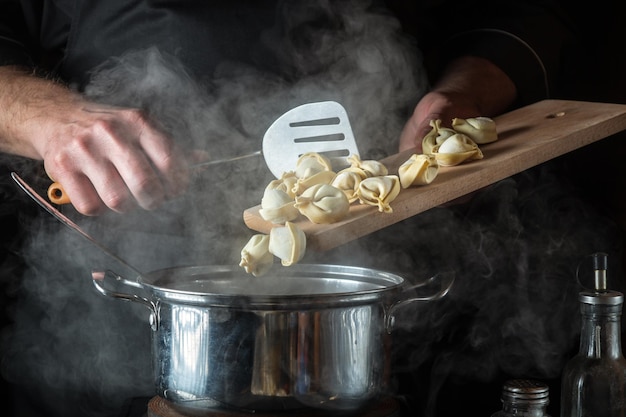 Chef prepara pelmeni em uma panela na cozinha do restaurante Closeup de mãos de cozinheiro enquanto trabalhava