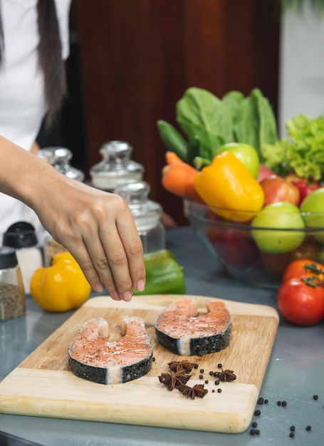 El chef prepara pescado de salmón fresco en una tabla de cortar de madera, una rodaja de salmón fresco, espolvorea con especias y hierbas provenzales con ingredientes. cocinar comida de pescado Cocinar cocina vegana.