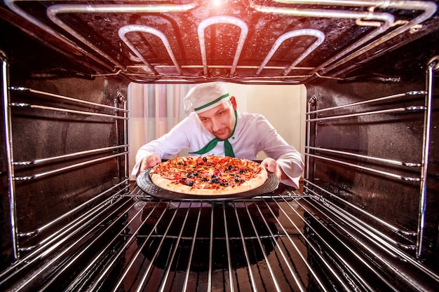 Chef prepara pizza en el horno, vista desde el interior del horno. Cocinar en el horno.