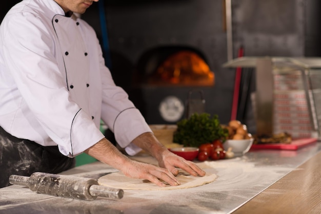 Chef preparando masa para pizza rodando con las manos espolvoreadas con mesa de harina