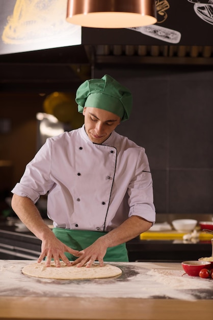 Chef preparando masa para pizza rodando con las manos espolvoreadas con mesa de harina