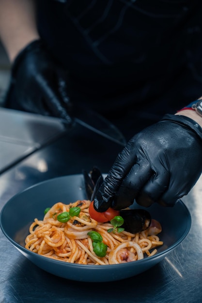 Chef preparando pasta de marisco con mejillones con albahaca y tomate en plato negro