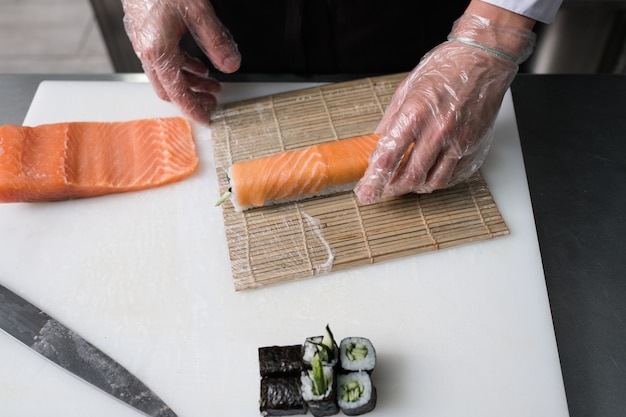Chef preparando rollos de sushi philadelphia cubriéndolos con trucha o salmón. Deliciosa comida de tradición culinaria asiática.