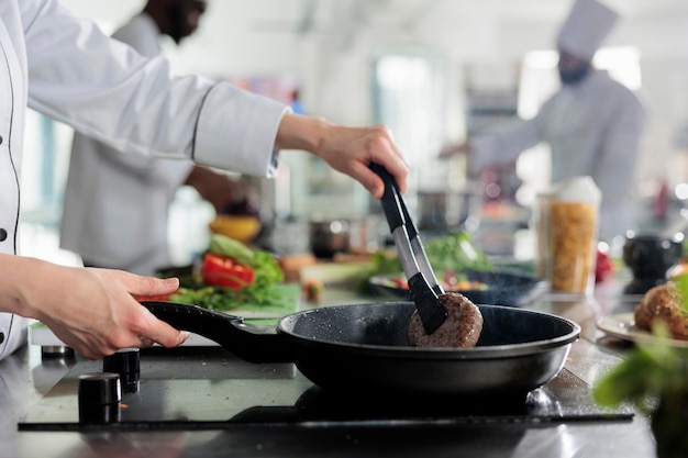 El chef principal cocina hamburguesas de ternera en una sartén caliente mientras cocina un plato gourmet para el servicio de cena. Trabajador calificado de la industria alimentaria que fríe carne picada en la cocina profesional del restaurante.