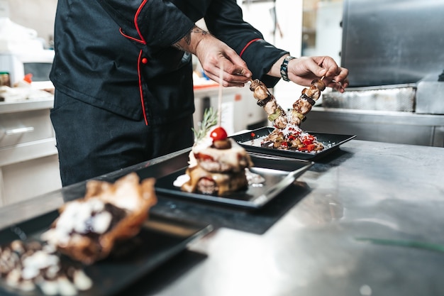 Chef profesional arreglando plato de comida con carne y verduras.