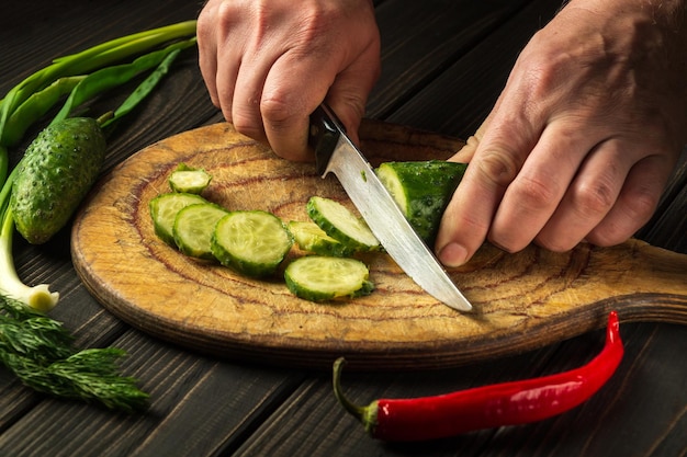 Chef profesional corta un pepino en una tabla para cortar