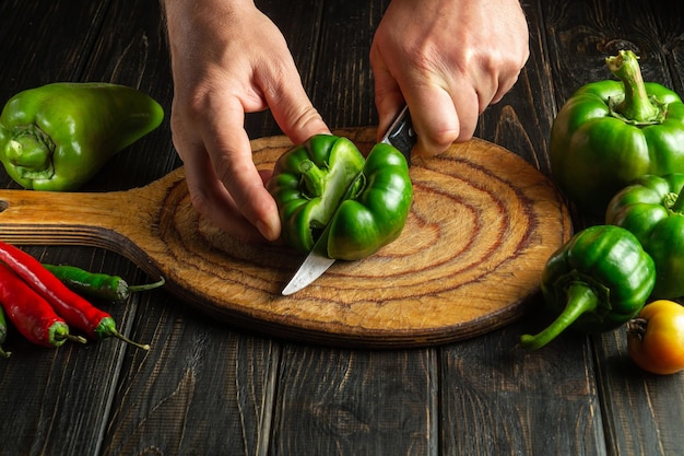 Chef profesional corta pimientos verdes frescos en una tabla de cortar de madera Primer plano de manos de cocinero mientras prepara comida vegetariana