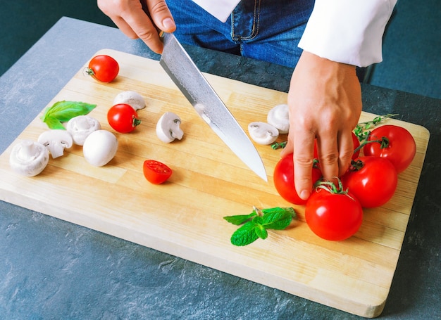 Chef profesional corta verduras con un cuchillo afilado de acero de Damasco. Técnica mixta