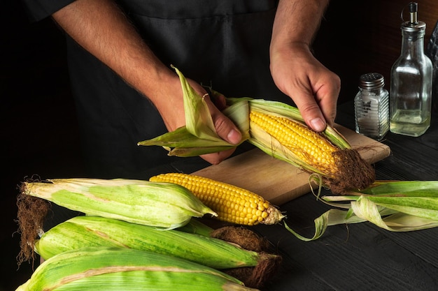 Chef profesional pela maíz maduro de la cáscara antes de cocinar