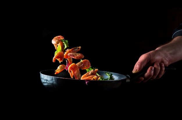 Chef profesional prepara camarones con hierbas. Cocinar mariscos, comida vegetariana saludable y comida sobre un fondo oscuro. Espacio publicitario gratuito