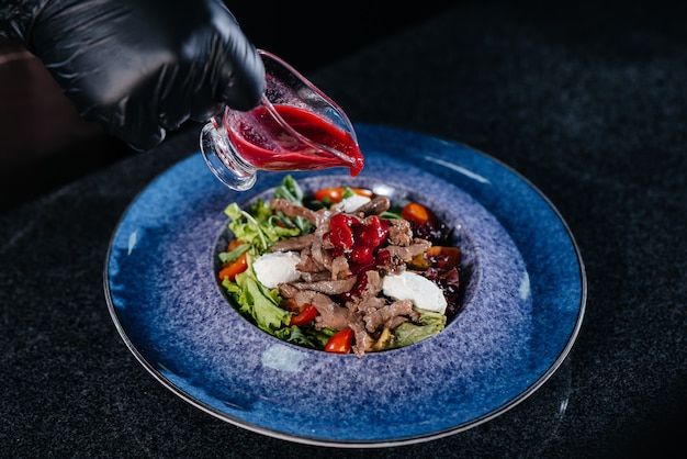 Un chef profesional prepara una deliciosa ensalada fresca de verduras y ternera jugosa en un restaurante moderno y elegante. Cocinar en un restaurante.