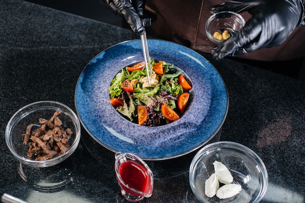 Un chef profesional prepara una deliciosa ensalada fresca de verduras y ternera jugosa en un restaurante moderno y elegante. Cocinar en un restaurante.