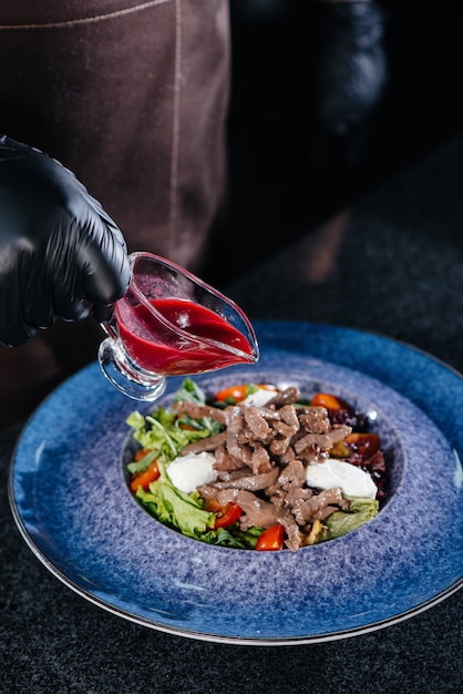 Un chef profesional prepara una deliciosa ensalada fresca de verduras y ternera jugosa en un restaurante moderno y elegante. Cocinar en un restaurante.