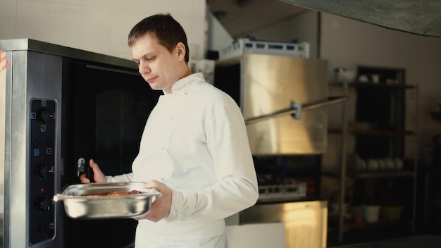 El chef profesional puso un plato de carne en el horno en la cocina del restaurante