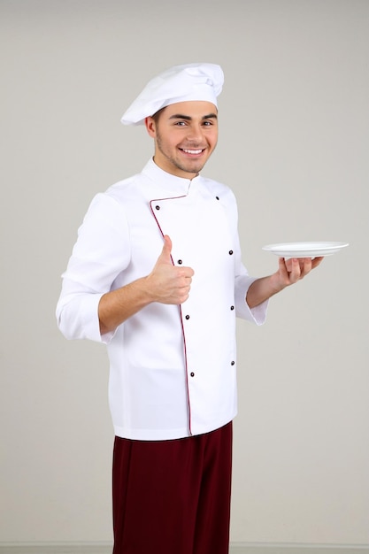 Chef profesional en uniforme blanco y sombrero sobre fondo gris
