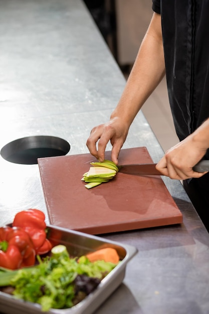 Chef profesional en uniforme preparando verduras frescas en la tabla de cortar en la cocina del restaurante Concepto culinario