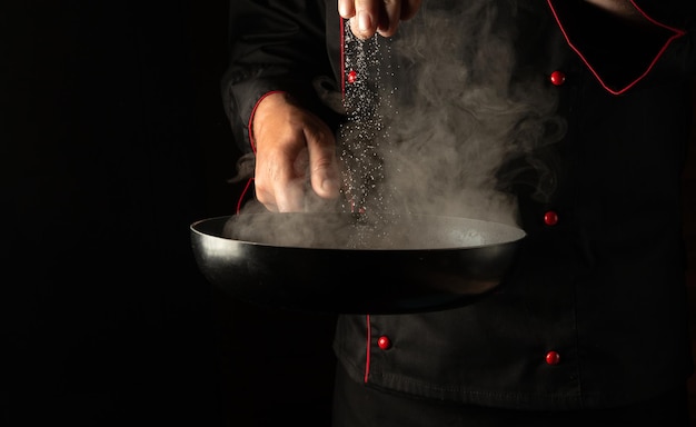 Chef profissional adiciona sal a uma panela quente com costeletas de hambúrguer de carne