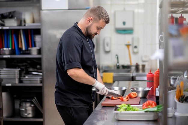 Chef profissional de uniforme corta legumes frescos na cozinha Cozinheiro cozinhando delicioso enfeite para clientes no restaurante Conceito culinário