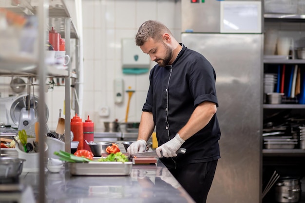 Chef profissional de uniforme corta legumes frescos na cozinha Cozinheiro cozinhando delicioso enfeite para clientes no restaurante Conceito culinário