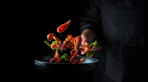 Chef profissional prepara camarão com ervas. cozinhar frutos do mar, comida vegetariana saudável e comida em um fundo escuro. espaço publicitário grátis