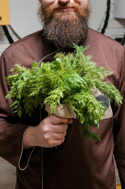 Chef con ramo de eneldo y perejil, hombre con barba, cocina, concepto de ensalada verde