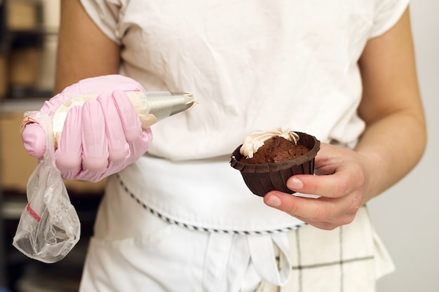 El chef de repostería aplica la crema al muffin de chocolate