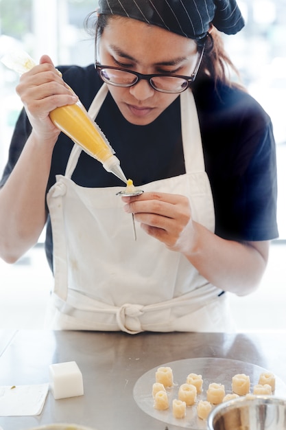 El chef de repostería de la mujer tiene la intención de hacer una flor de mantequilla amarilla para la decoración de pasteles.