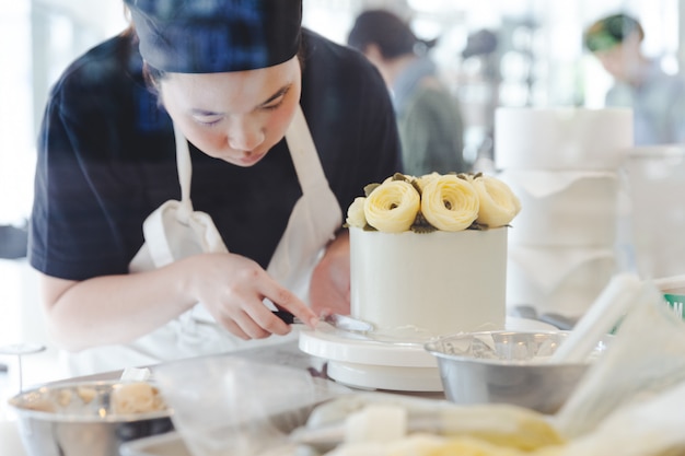 Chef de repostería que hace una flor amarilla de la mantequilla para la decoración de la torta.