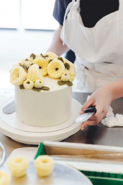 Chef de repostería que hace una flor amarilla de la mantequilla para la decoración de la torta.