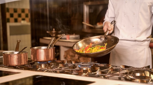 Chef de restaurante cocinando rodajas de pimiento en una sartén