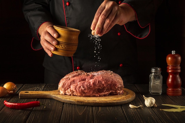 El chef rocía la carne cruda con sal.