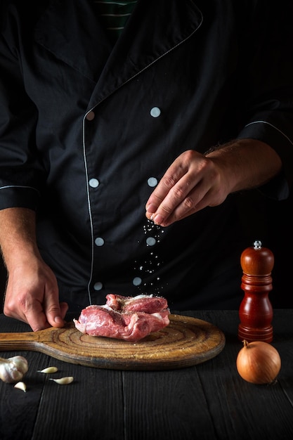 El chef rocía la carne con sal Preparando la carne antes de hornear