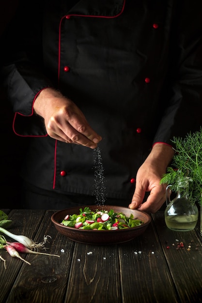 El chef rocía sal a la ensalada de verduras frescas en el plato Preparando comida saludable en la cocina