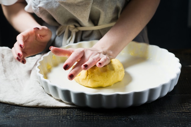 Chef rollt den Teig in einer Auflaufform aus und kocht. Seitenansicht