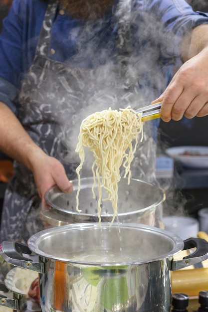 El chef saca con la cuchara ranurada los fideos de huevo al vapor calientes de la sartén