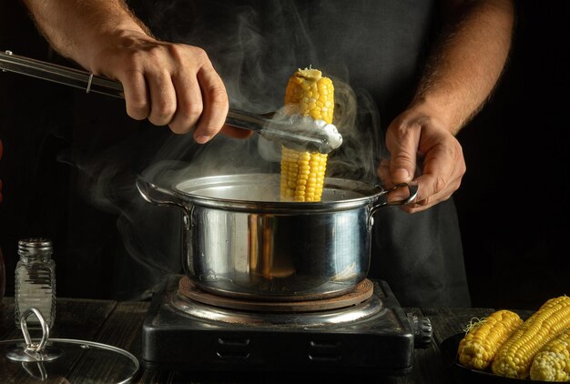 El chef saca la mazorca de maíz caliente de la olla con pinzas en la cocina