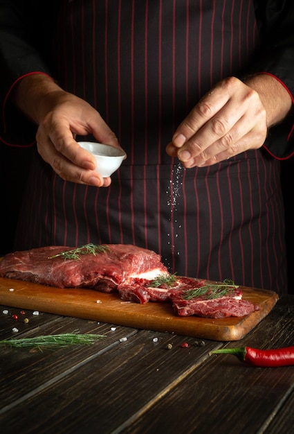 El chef sala la carne antes de freírla o asar Ternera fresca en la mesa de la cocina