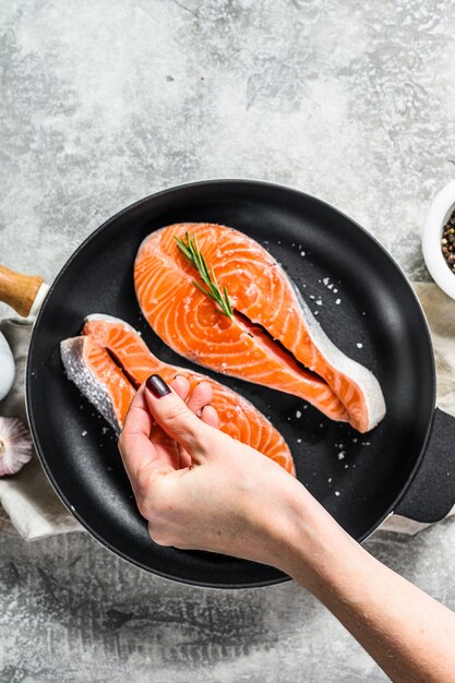 Chef salzt rohes Lachssteak in einer Pfanne. Gesunde Meeresfrüchte. Draufsicht ..