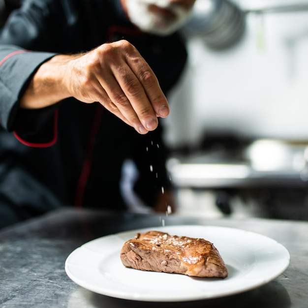 Foto chef sazonando el bistec en la cocina profesional