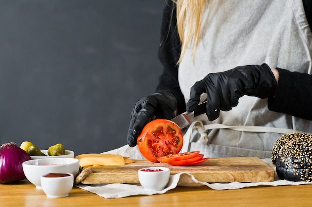 Chef schneidet rote tomaten. das konzept, einen schwarzen burger zu kochen.