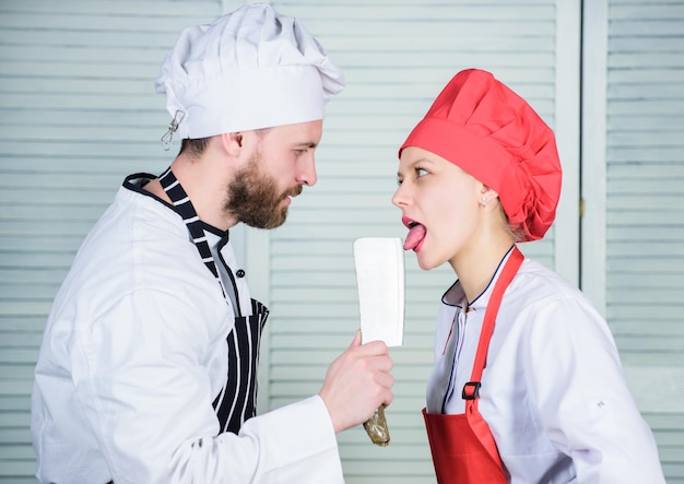 Chef segura a ferramenta de faca de cutelo enquanto a mulher lambe a lâmina. Cozinhar é sexy. Ferramenta profissional de faca afiada. O homem usa uma faca afiada de cutelo. Casal brincalhão com faca perigosa. Lâmina de metal. Lambida perigosa.