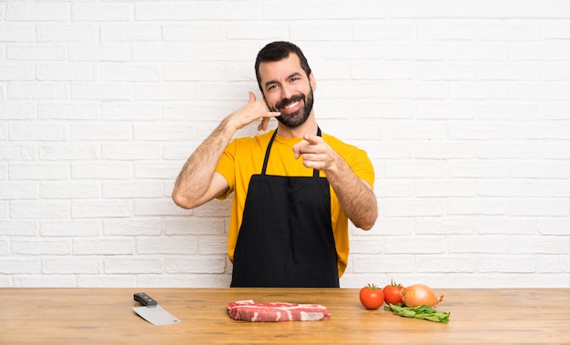 Chef, segurando em uma cozinha fazendo gesto de telefone e apontando a frente