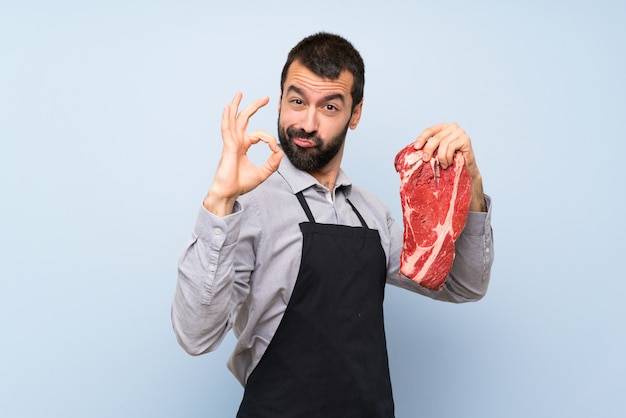 Foto chef segurando uma carne crua, mostrando sinal de ok com os dedos