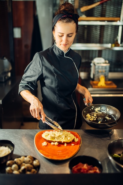 Chef de sexo femenino con pan para cocinar carne con pasta en la mesa de madera. Adorne para bistec, preparación de alimentos en la cocina