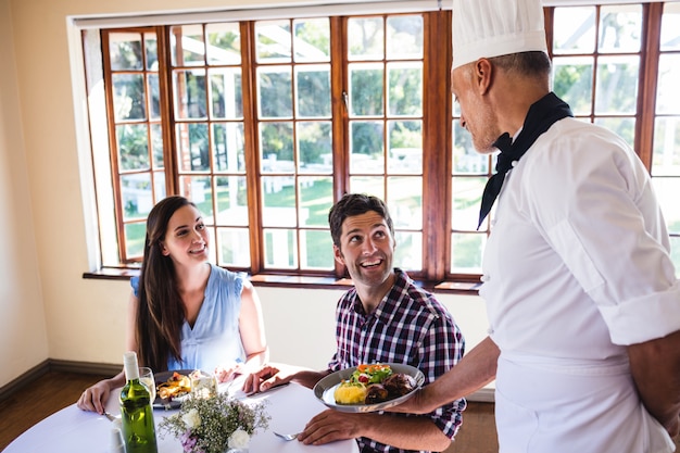 Chef sirviendo comida a la joven pareja sentada en un restaurante