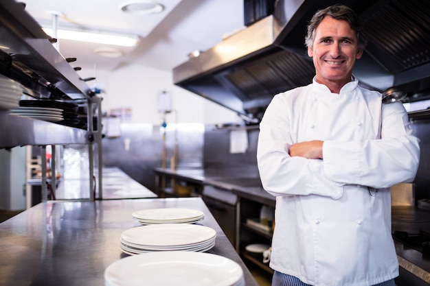 Foto chef sorridente com as mãos cruzadas na cozinha