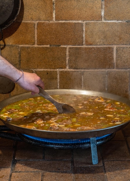 Chef sosteniendo una cuchara de madera revolviendo el arroz de una auténtica pella valenciana en una cocina rústica