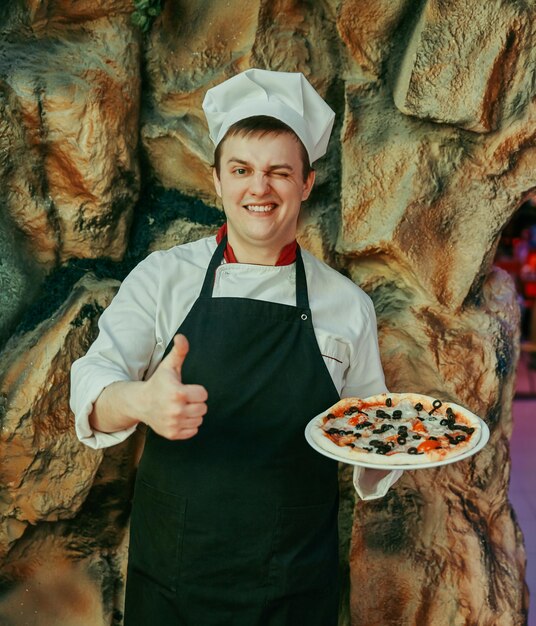 Chef sostiene una pizza grande y muestra un pulgar hacia arriba