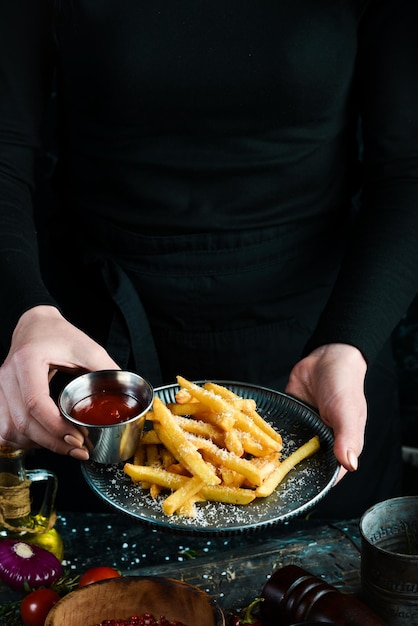 El chef sostiene un plato de papas fritas con queso y salsa en una placa de metal sobre un fondo rústico de madera Concepto de comida rápida