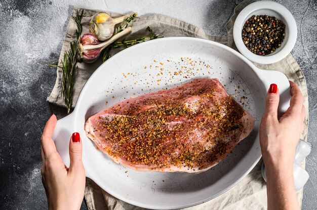 Chef sostiene una sartén con cortes de carne de cerdo fresca. Carne cruda con especias. Fondo gris Vista superior.